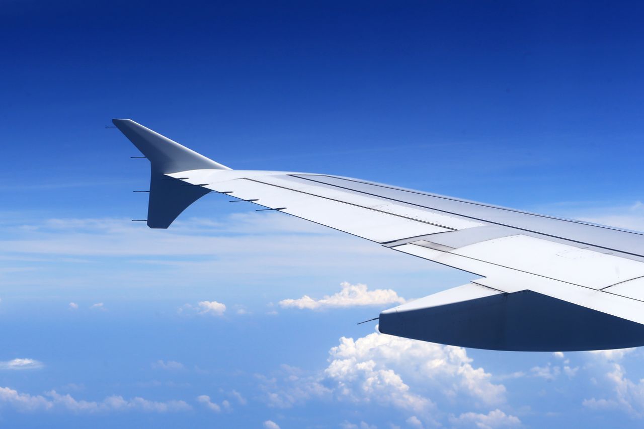 services-01 A stunning view from an airplane window showing a wing against a clear blue sky and clouds.