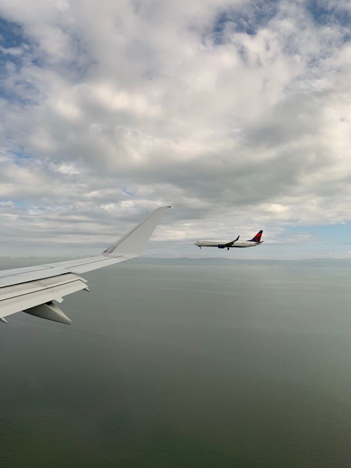 contact-hero Airplane flying over open water with a clear sky, captured from another aircraft.