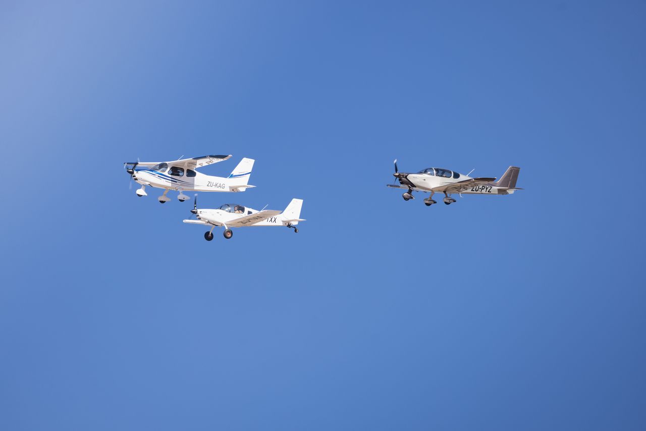 role-01 Three light aircraft flying in formation against a clear blue sky, showcasing aviation precision.